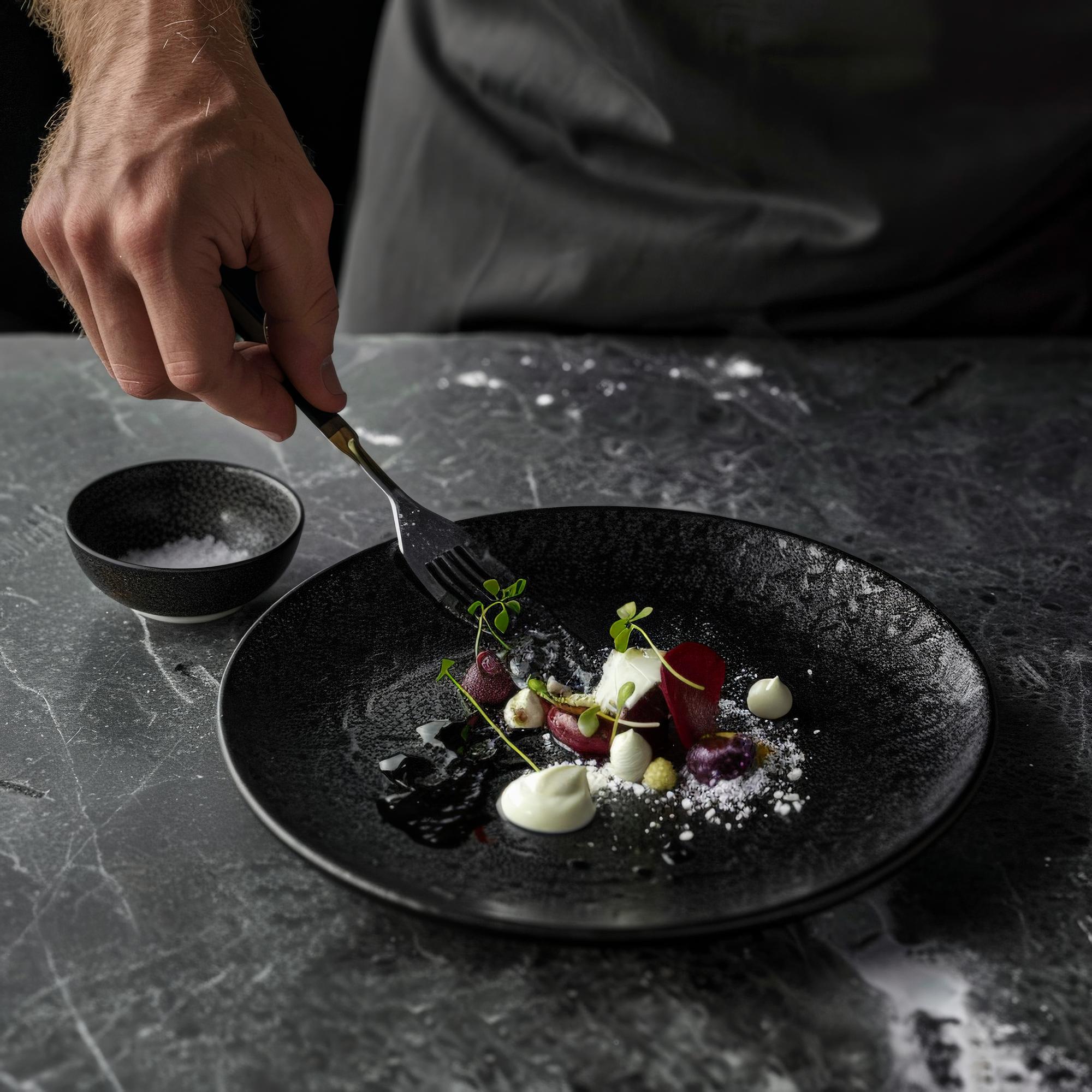 Chef plating a fine dish on a dark linen